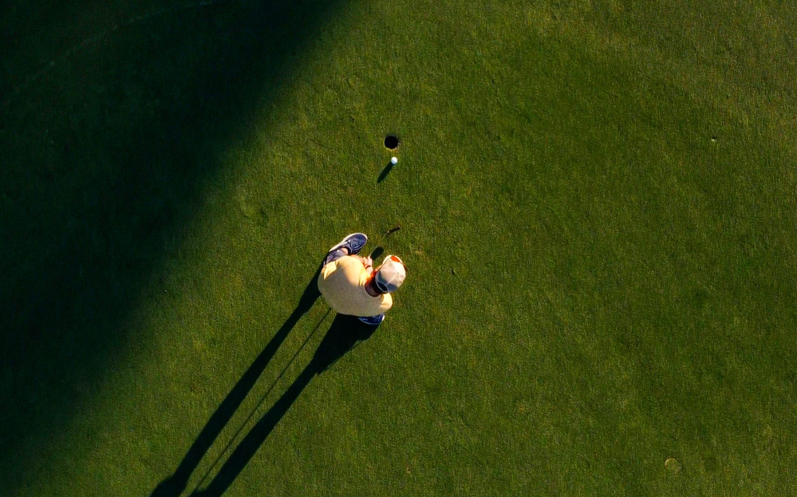 Aerial view of man putting golf ball on the golf green into the hole.